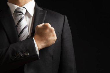 Siyah takım elbiseli iş adamı, siyah arka planda sol göğsüne yumruk atarak güven gösteriyor.