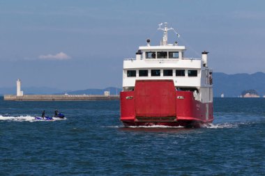 Büyük kırmızı feribot açık mavi gökyüzünün altında limana yaklaşıyor.