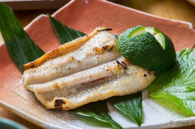 Izgara beyaz balık filetoları yeşil yaprakların üzerinde dinleniyor.