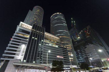 Aydınlatılmış modern gökdelenler geceleri şehir sokağının üzerinde yükseliyor.
