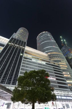 Aydınlatılmış modern gökdelenler geceleri şehir sokağının üzerinde yükseliyor.