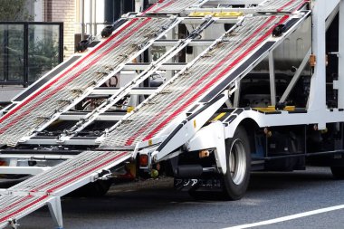 Şehir sokağının yanına park edilmiş metalik otomobil rampası görünüyor.