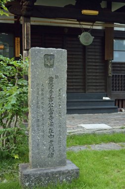 Geleneksel ahşap binanın yanında Japon yazıtları bulunan taş heykel.