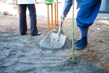 Dışarıda kürek kullanarak çimento döşeyen iki kişi.