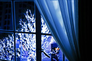 Noel arkaplanı, güzel perdeleri ve ışıklandırılmış çelenkleri olan neşeli bir ağacı var.              