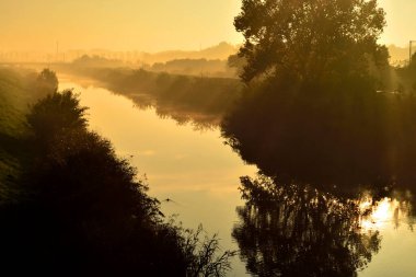 Nehir üzerinde güzel bir gün doğumu, tarla ve ağaçlar sisli bir sabahta