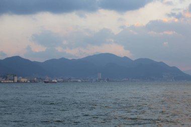 Deniz kıyısında gün batımı, şehir silüeti ve akşamları tepeler. 