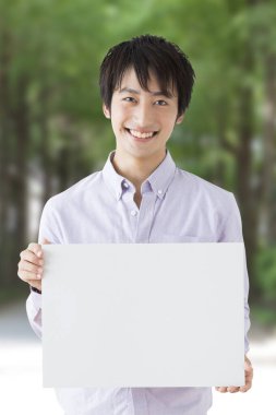 Asyalı genç adam boş ilan panosu tutuyor ve gülümsüyor. 