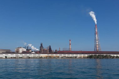 Suyun yakınındaki sanayi binaları berrak mavi gökyüzü altında