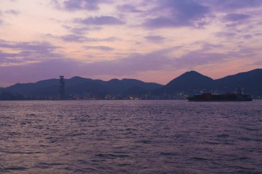 Deniz kıyısında gün batımı, şehir silüeti ve akşamları tepeler. 