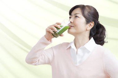 Asyalı olgun bir kadın yeşil meyve suyu içiyor, sağlıklı bir yaşam tarzı.