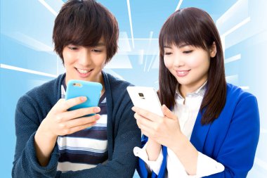 Asyalı genç çift cep telefonu kullanıyor ve gülümsüyor.