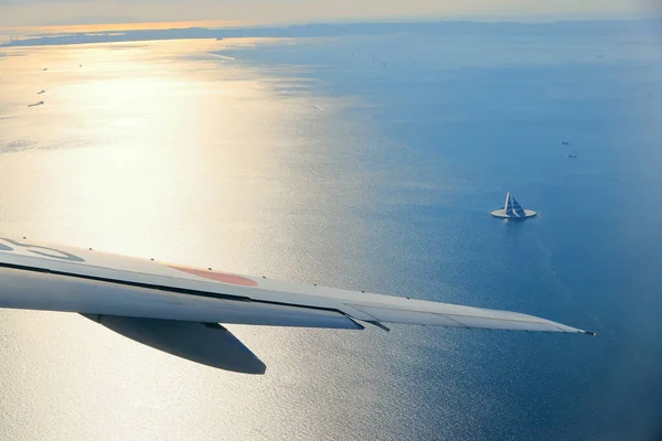 view of an airplane flying over the sea with boats