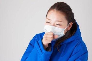 Beyaz arka planda tıbbi maskesi olan mavi ceketli güzel bir Japon kadının portresi.