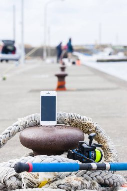 Akıllı telefon, eski deniz ipi ve deniz kıyısındaki olta kamışı.