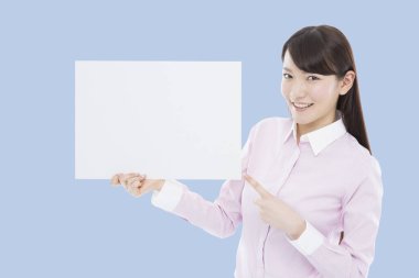 Elinde boş afiş tutan ve kameraya gülümseyen bir kadın.