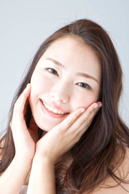 Güzel gülümseyen Asyalı kadın yüzüne dokunuyor