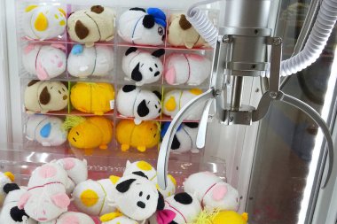 Kazanmayı bekleyen renkli peluş oyuncaklarla dolu bir pençe makinesi.