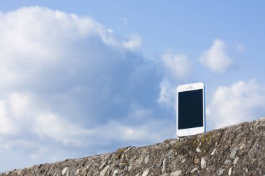 Plaj taşları üzerinde boş ekranlı akıllı telefon mavi gökyüzüne karşı, boşluğu kopyala