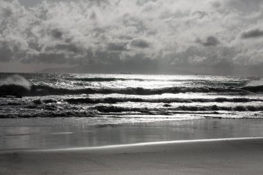 Kumlu kumlu bir plajın gri renkli bir görüntüsü ve bulutlu bir gökyüzü.