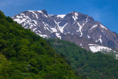 Dağları, yeşil ağaçları ve mavi gökyüzü olan güzel bir manzara.