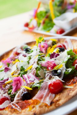 Tahta bir masada jambonlu, sebzeli ve peynirli İtalyan pizzası. 