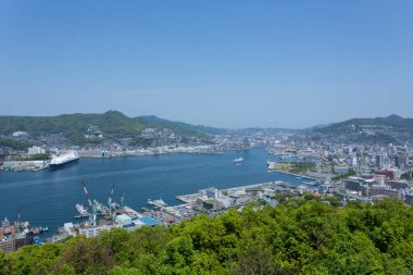 Açık gökyüzünün altındaki uzak dağlarla birlikte liman şehri manzarası