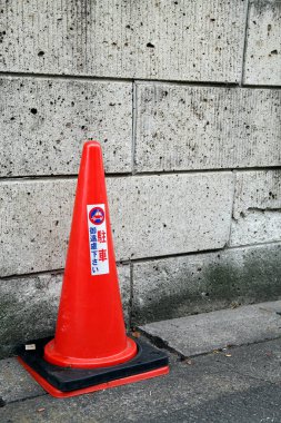 Parlak turuncu trafik konisi desenli beton duvarın yanında duruyor