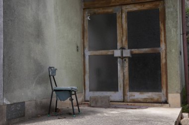 Gri duvara yaslanmış eski ahşap sandalye. Arka planda görünen bir kapı var..