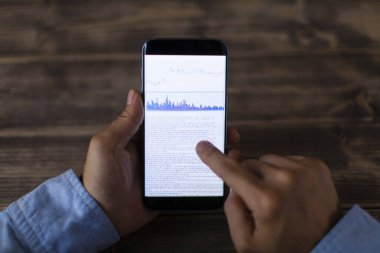 Telefon ekranında mali istatistik grafikleri olan akıllı telefon kullanan bir işadamı.