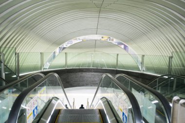 Parlak kıvrımlı tünel yapısının içinde alçalmakta olan modern yürüyen merdiven