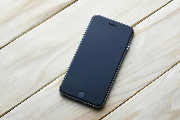 black smart phone with blank screen for text on wooden background.