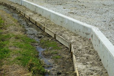 Çamurlu inşaat alanının yanındaki çakıl taşı sınırında beton kaldırım.