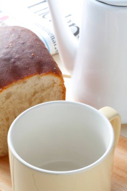 Bir somun ekmek, kahve fincanı ve beyaz su ısıtıcısının yakın çekimi.