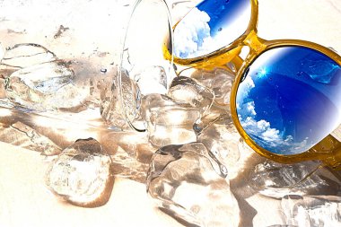 Beyaz zemin üzerinde buz küpleri ve sarı güneş gözlüğü olan bir bardak su, güneşli bir günde yaz tatili ve rahatlama kavramı, kopyalama alanı