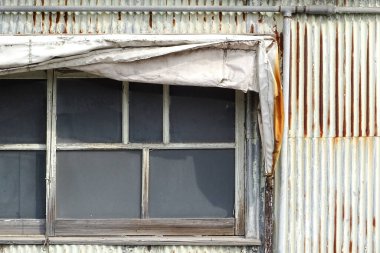 Yıpranmış metal duvar, eski pencere ve yırtık tente.