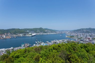 Sahil kenti limanına bakan yeşil tepeler ve mavi gökyüzü