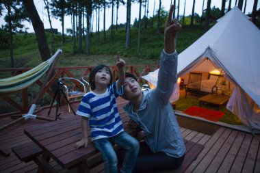 Asyalı çocuk ve babası ormanda kamp yaparken çadırın yanındaki masada oturuyorlardı. 