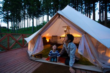 Asyalı çocuk ve babası gökyüzüne bakıyorlar ormanda kamp yaparken çadırda oturuyorlar. 