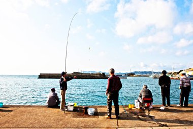 Erkekler güneşli bir günde deniz kıyısında balık tutuyorlar.