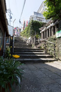 Parlak güneş ışığı altındaki binaların arasından yukarı doğru çıkan taş adımlar.