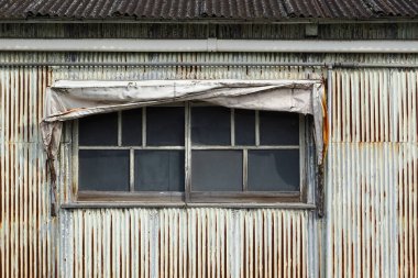 Yıpranmış metal duvar, eski pencere ve yırtık tente.