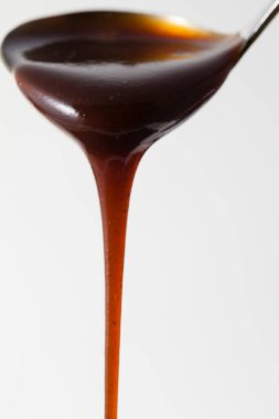 Beyaz arka planda kepçeden akan koyu siyah sos.