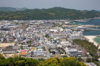 Yeşil tepeler ve sahil kenarındaki sahil şehir binalarına bakıyorum.