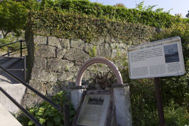 Metal korkulukların ve dışarıdaki bilgilendirme işaretlerinin yanında tarihi taş duvar.