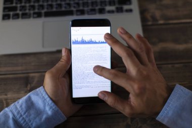 Telefon ekranında mali istatistik grafikleri olan akıllı telefon kullanan bir işadamı.