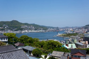 Sahile bakan şehir manzarasında çatılar su tepeleri yeşil gökyüzü