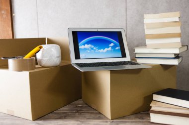 Tahta masanın üzerinde bir yığın karton kutu olan dizüstü bilgisayar.