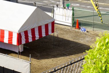 Çizgili olay çadırı sokağın yanındaki boş toprak arazinin yanında duruyor.
