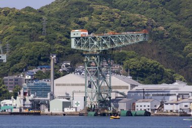 Büyük endüstriyel vinç yeşil tepelerin arasında fabrika binalarının yanında duruyor.